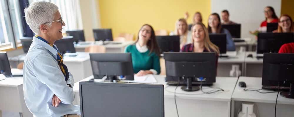 Profesor acompaña una clase de adultos en un aula de informática.